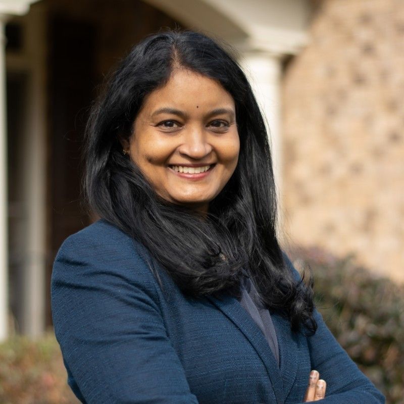 Smiling professional in a blue blazer with arms crossed, standing outdoors in front of a stone building.