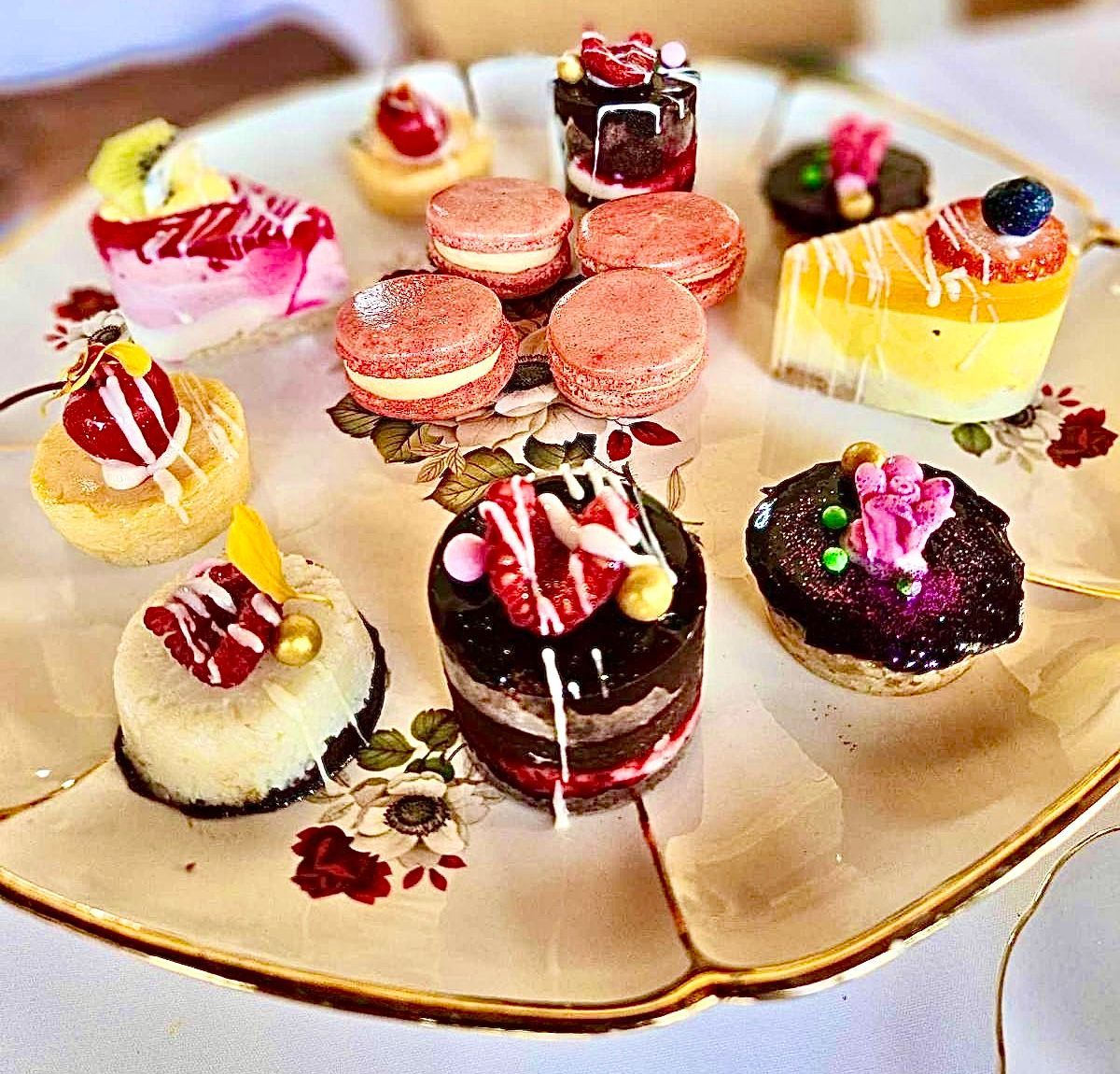 Assorted miniature desserts on a decorative floral plate; includes macarons, cakes, and pastries — My Rainbow Bakery, Cafe & Catering in Cannonvale, QLD