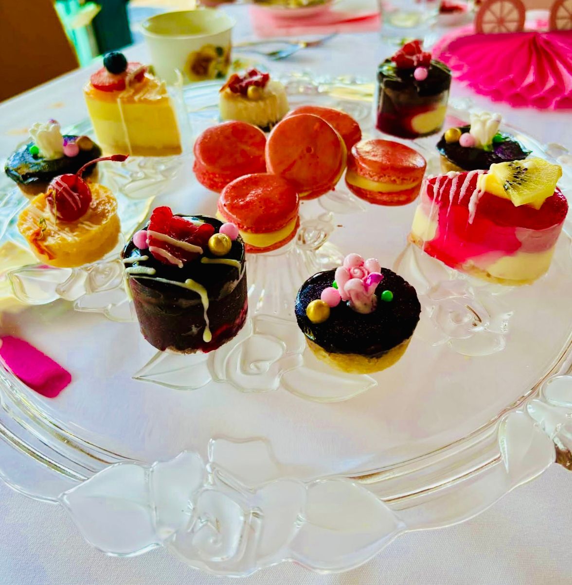 Dessert display: Various small cakes and macarons on a clear, tiered serving plate on a table with a white cloth — My Rainbow Bakery, Cafe & Catering in Cannonvale, QLD