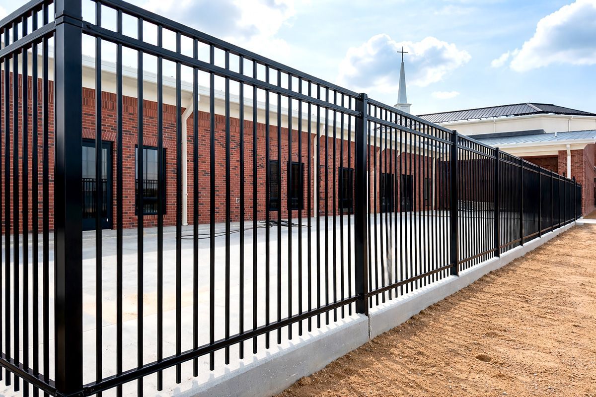 Black metal fence surrounding a brick building with a steeple.
