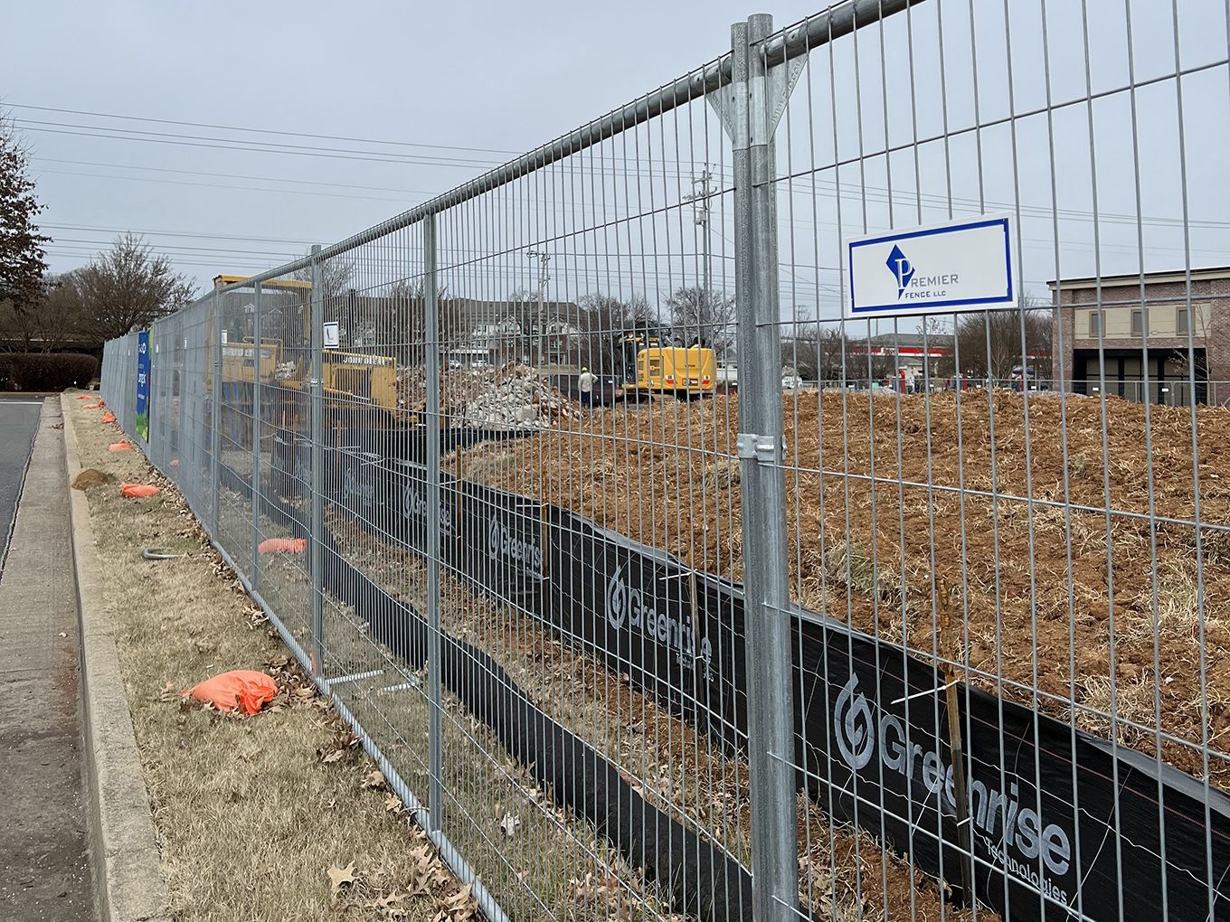A fence surrounds a construction site with a bulldozer in the background.