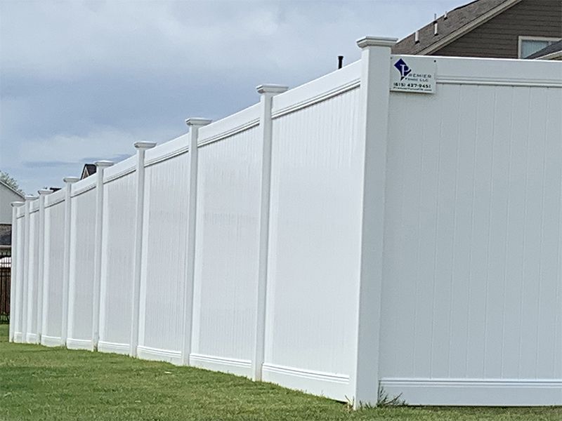 White vinyl privacy fence in a grassy yard under a cloudy sky.