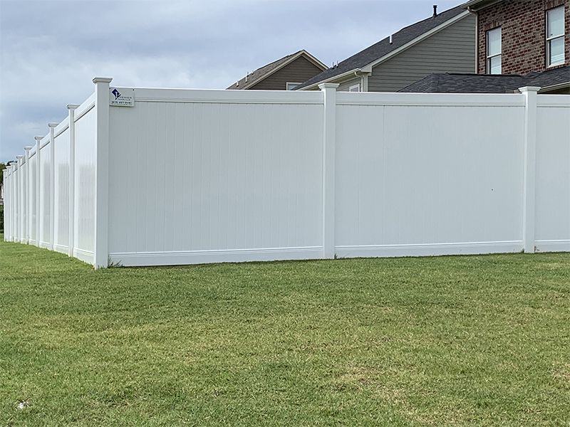 A white fence surrounds a lush green lawn in front of a house.