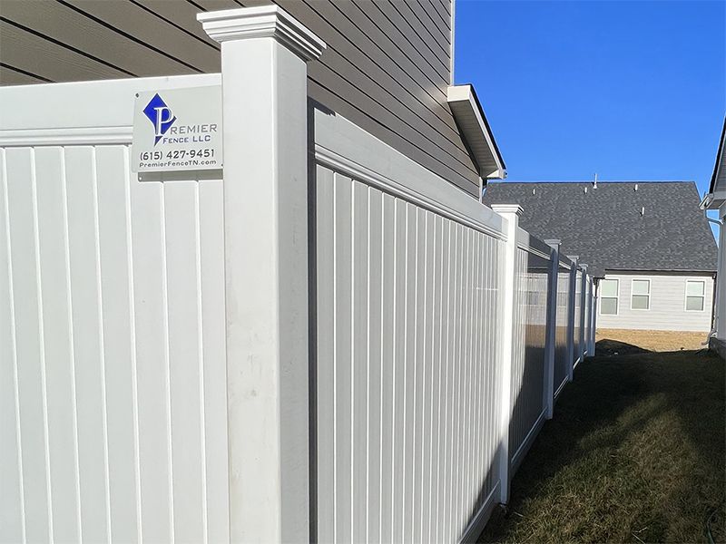 White vinyl fence bordering a house and yard on a sunny day.
