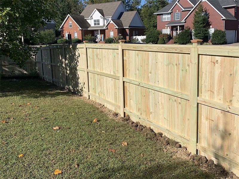 Wooden fence bordering a grassy yard with houses in the background on a sunny day.