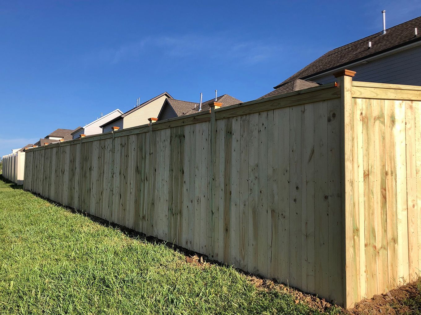 A wooden fence surrounds a grassy field in front of a house.