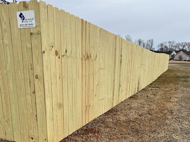 Wooden fence in a field, curved to the right. A company sign is attached to the fence. Cloudy sky.
