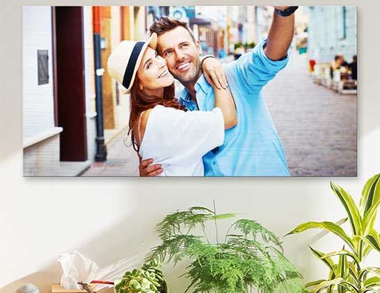 Smiling couple taking a selfie in a bright room, with plants in the foreground.