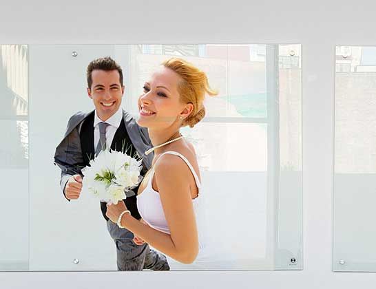 Smiling couple in wedding attire, holding a bouquet in a bright indoor setting