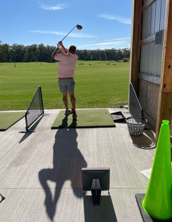 Person swinging a golf club at a driving range on a sunny day.