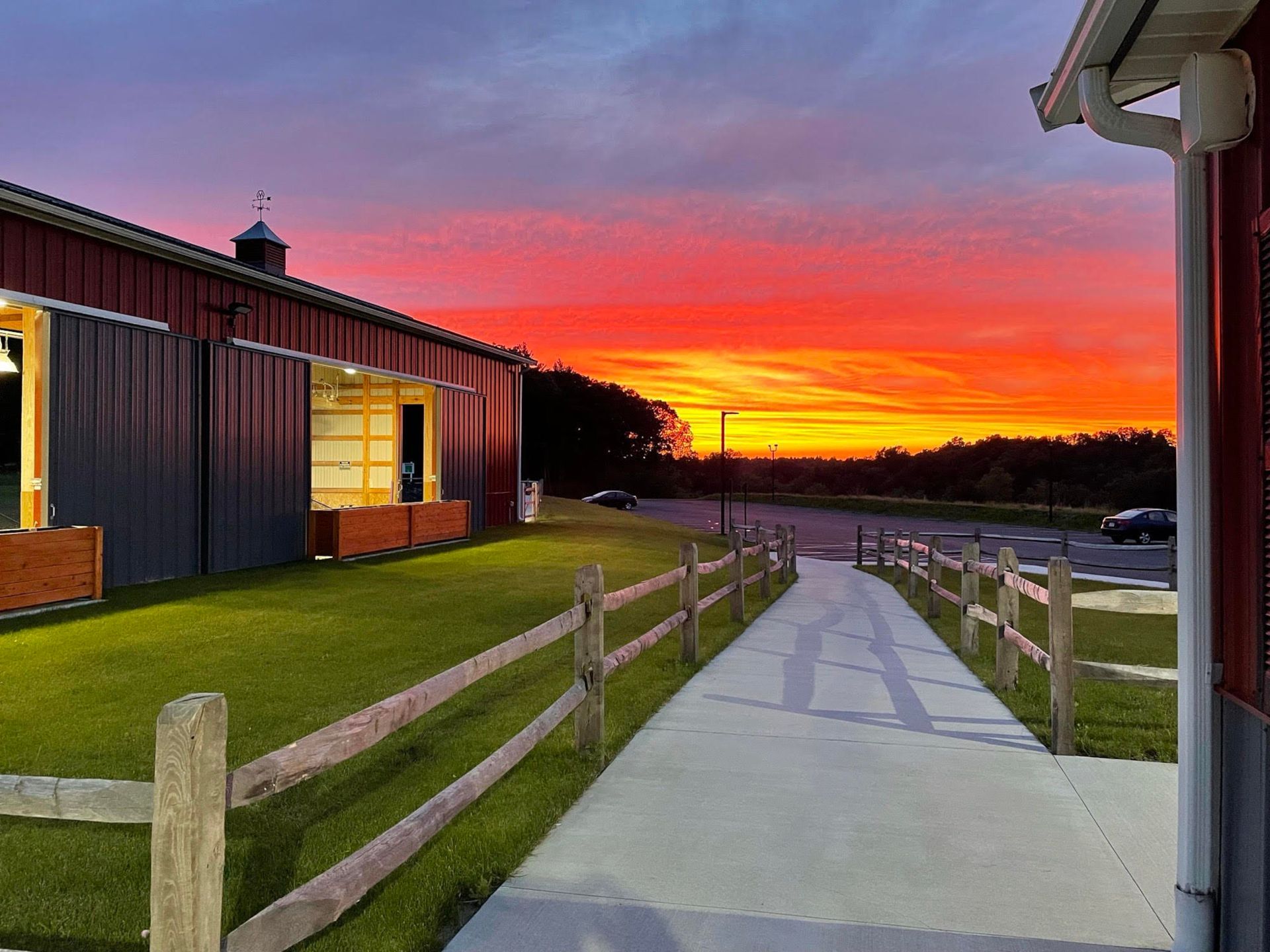 Barn at sunset, with a fiery red and orange sky over a concrete walkway and wooden fence.