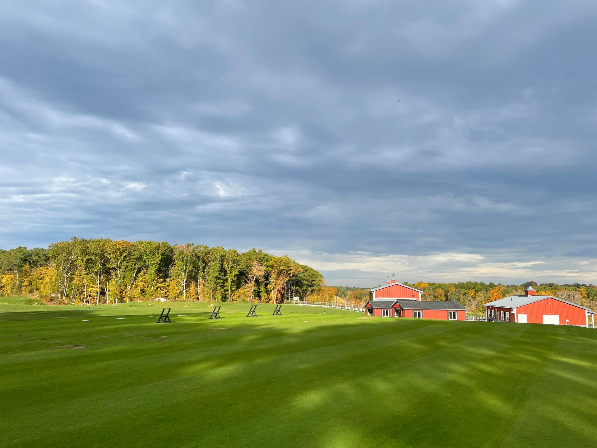 Green golf course with red buildings and trees under a cloudy sky.
