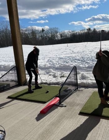 Person swings golf club at outdoor driving range covered in snow.