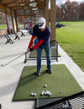 Man swinging a golf club at a driving range, wearing a white hat and jeans.