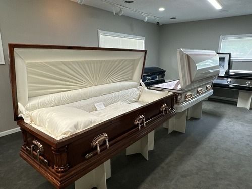 Open caskets displayed in a funeral home showroom, one dark wood and one white, both upholstered inside