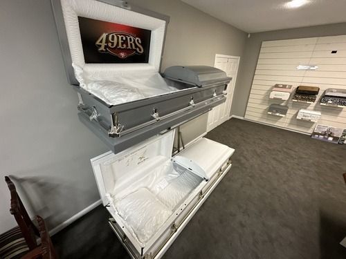 Display room with a wall-mounted casket and white display casket beneath a 49ers sign