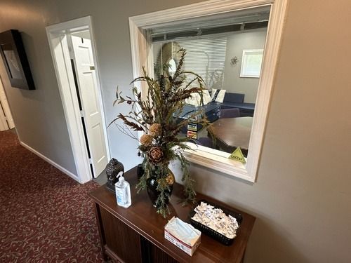 Hallway table with floral arrangement, decorative items, and a pass-through window into an office seating area.