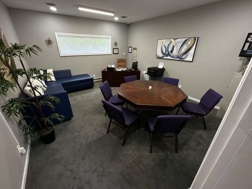 Small meeting room with round table, purple chairs, blue sofa, and wall art on gray carpet