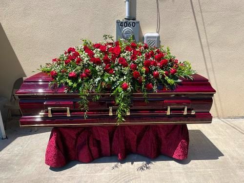 Maroon casket with red and white flower arrangement on a draped stand outdoors