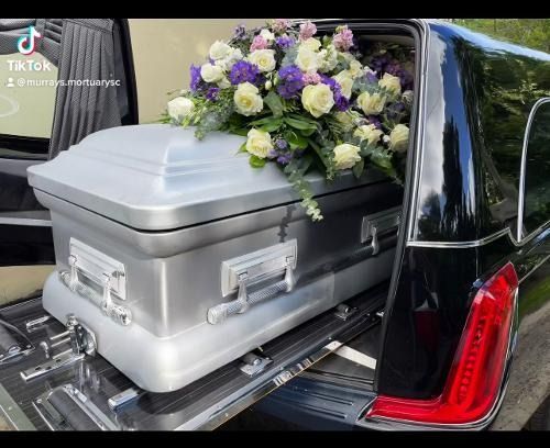 Silver casket with purple and white flowers in the back of a black hearse