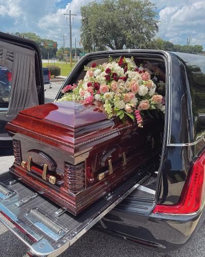 Casket with pink and white flowers in the open back of a black hearse outdoors