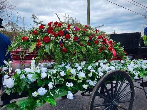 Flower-covered wagon with red and white blooms outdoors under a cloudy sky