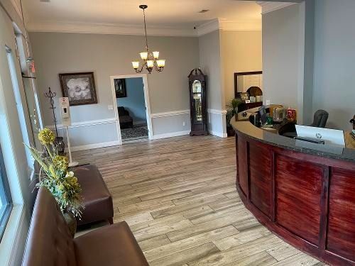 Spacious lobby with hardwood floor, chandelier, curved wooden reception desk, and seating area.