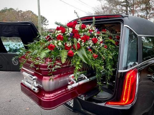Casket covered with red and white flowers, loaded into a black hearse