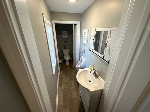 Narrow bathroom hallway with white sink, mirror, and toilet at the end