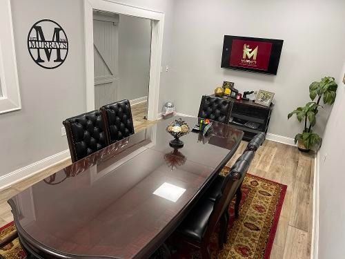 Modern conference room with long wooden table, black chairs, wall TV, and red patterned rug.