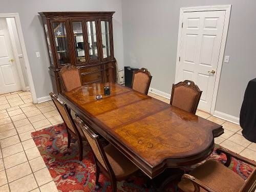 Dining room with a polished wooden table, four chairs, china cabinet, and patterned rug on tile floor.