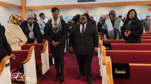 People standing in a church aisle among red pews during a service or gathering