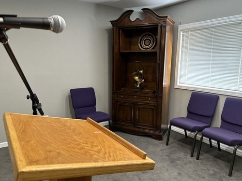 Podium with microphone in a small room with chairs and a wooden cabinet for records