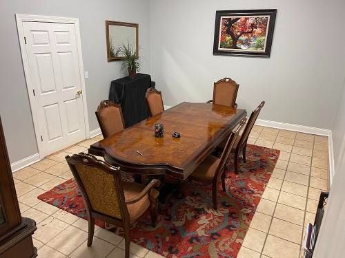 Dining room with wooden table, six chairs, tiled floor, red rug, and wall art.