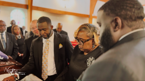 People standing in a church during a solemn ceremony, heads bowed in prayer.