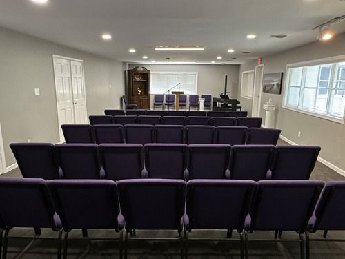 Small chapel or meeting room with rows of purple chairs facing a front stage and pulpit