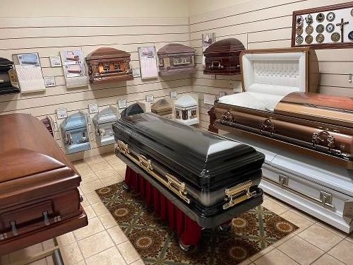 Coffin showroom with multiple polished caskets displayed on shelves and pedestals.