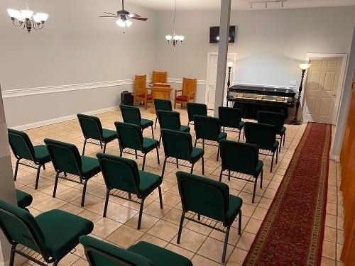 Empty church hall with rows of green chairs facing a piano and lectern.