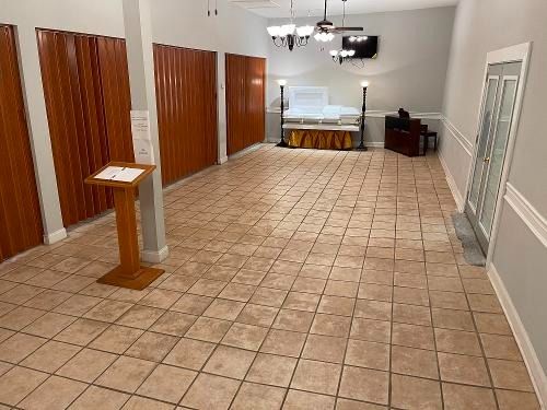 Empty tiled hall with wooden doors, white walls, a podium, and tables at the far end