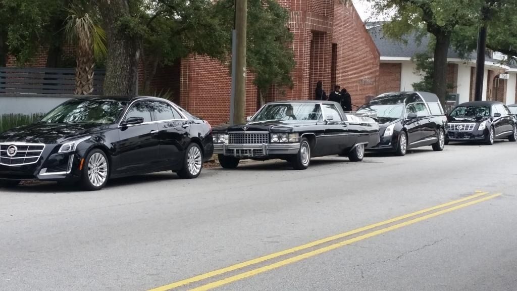 Parked black and white cars lined along a curb beside a brick building on a city street.