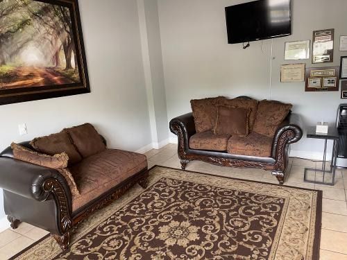 Living room with two brown sofas, patterned rug, wall art, and a mounted TV