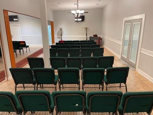 Empty conference room with rows of green chairs, white walls, and a tiled floor