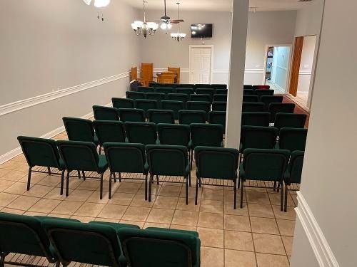 Empty meeting room with rows of dark green chairs, tiled floor, and a white column near the front.