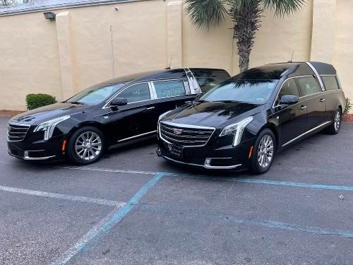Two black sedans parked side by side in a parking lot with a tan wall behind them