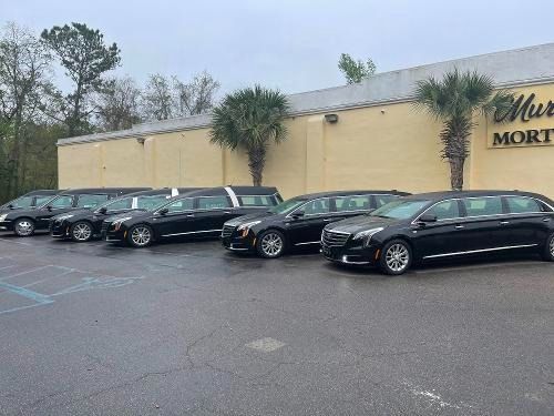 Black limousines lined up outside a beige building on a rainy parking lot