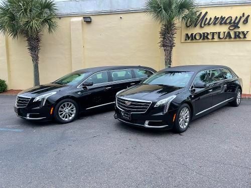 Two black hearses parked outside Murray's Mortuary at a beige building