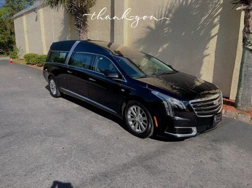 Black sedan parked on a sunny driveway beside a beige wall, with a watermark near the top.