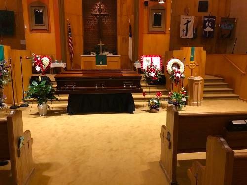 Church altar with candles, floral wreaths, and a black-draped table in a wooden sanctuary