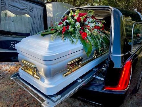 White casket with floral spray in black funeral hearse with red interior