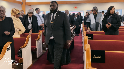 People standing in a church sanctuary between red pews during a solemn service